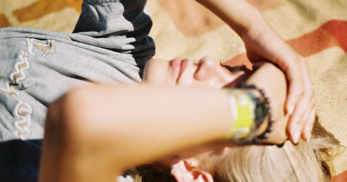Woman sick during her vacation, she lies outside on a beach towel with her hand on her forehead.