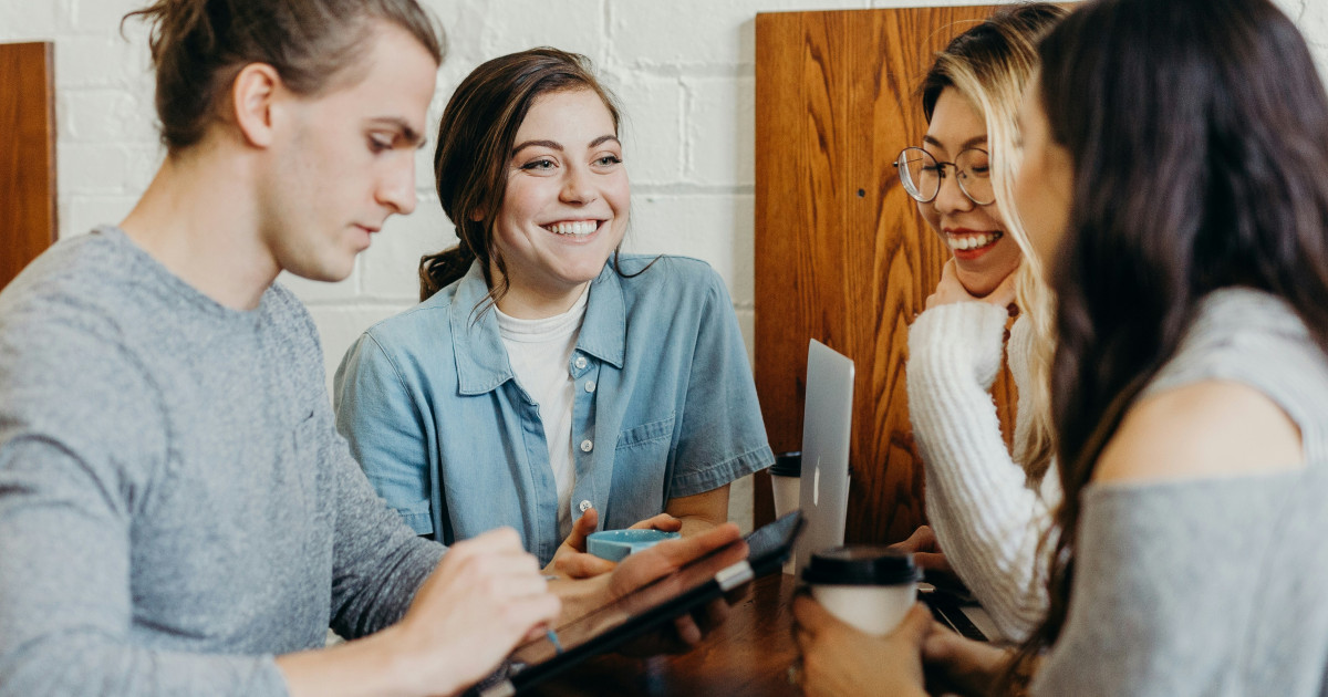 Vier mensen overleggen samen aan een tafel met laptops en een tablet.