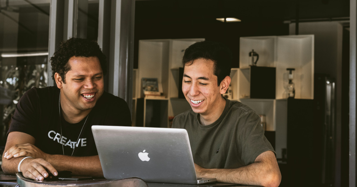 Two colleagues laughing together while looking at a laptop.