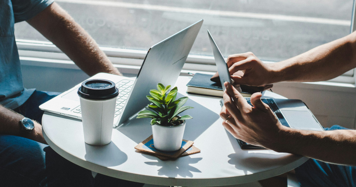 Two people work together at a round table with laptops and coffee.