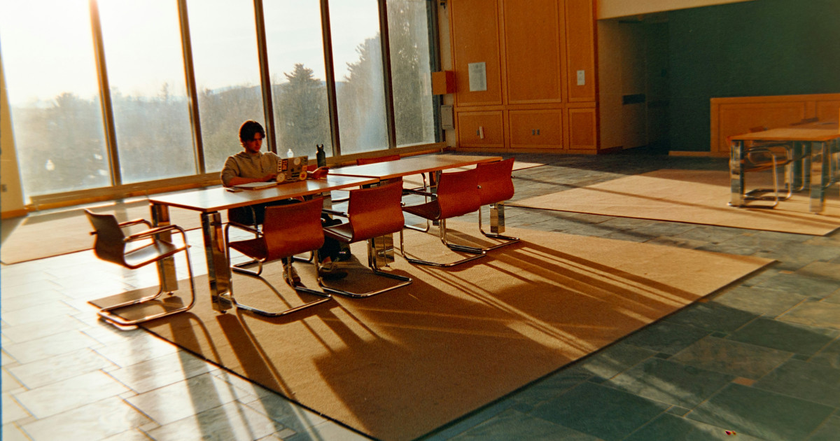Person sitting alone at a large conference table, with sunlight streaming in through tall windows.