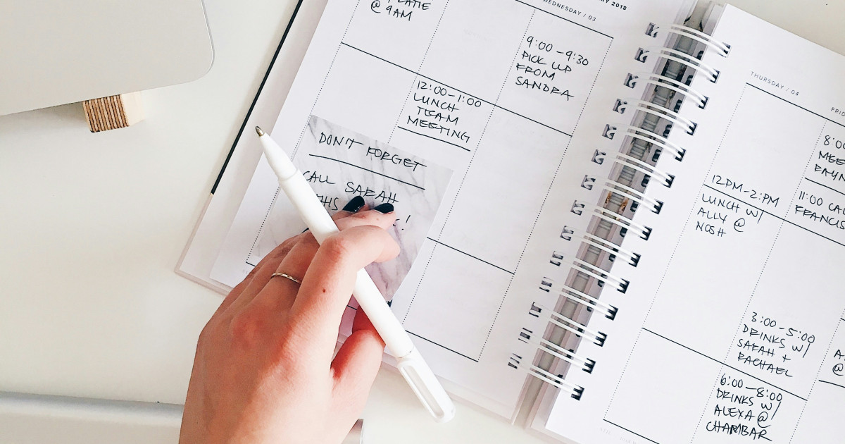 Hand writing in a weekly planner next to a laptop and keyboard.
